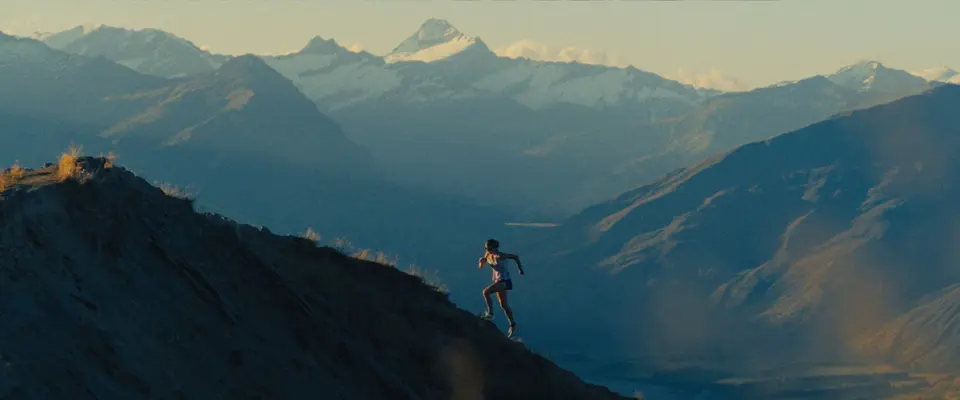 Ruth running up a ridge above snowy peaks. Still from ROOTS, Alexis Berg / Little Hell